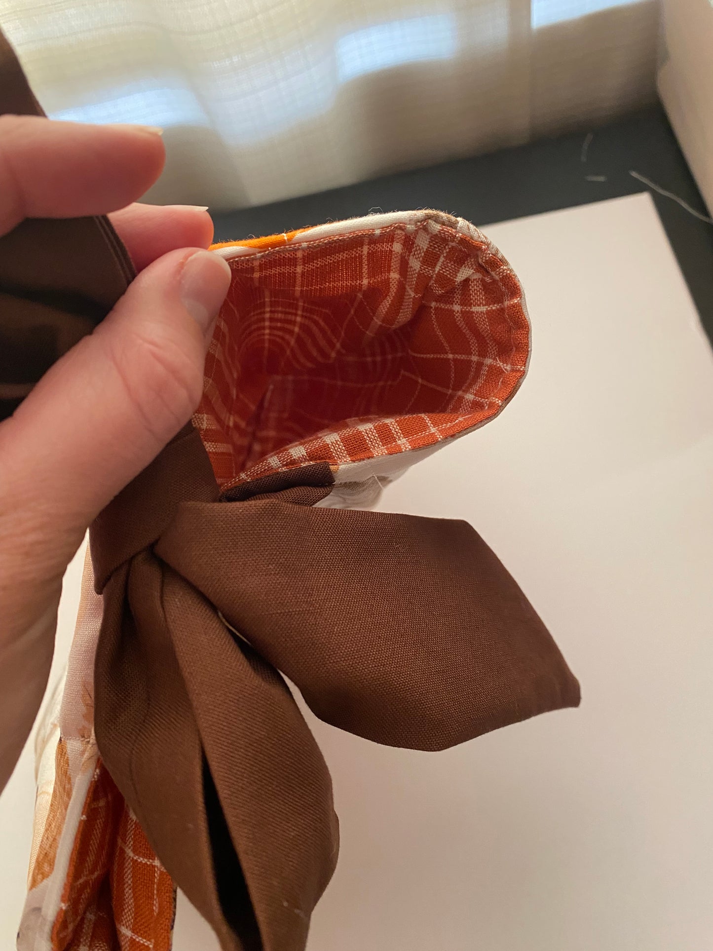 Hand holding a brown fabric flower with a checkered center against a neutral background