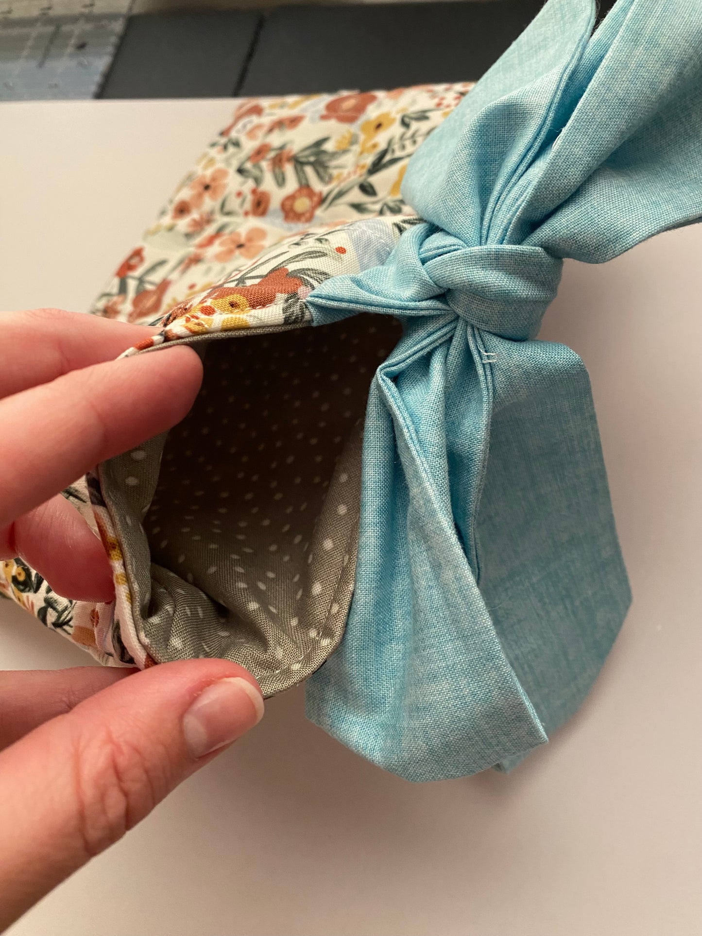 Hand holding a book sleeve with floral and polka dot patterns on a neutral background