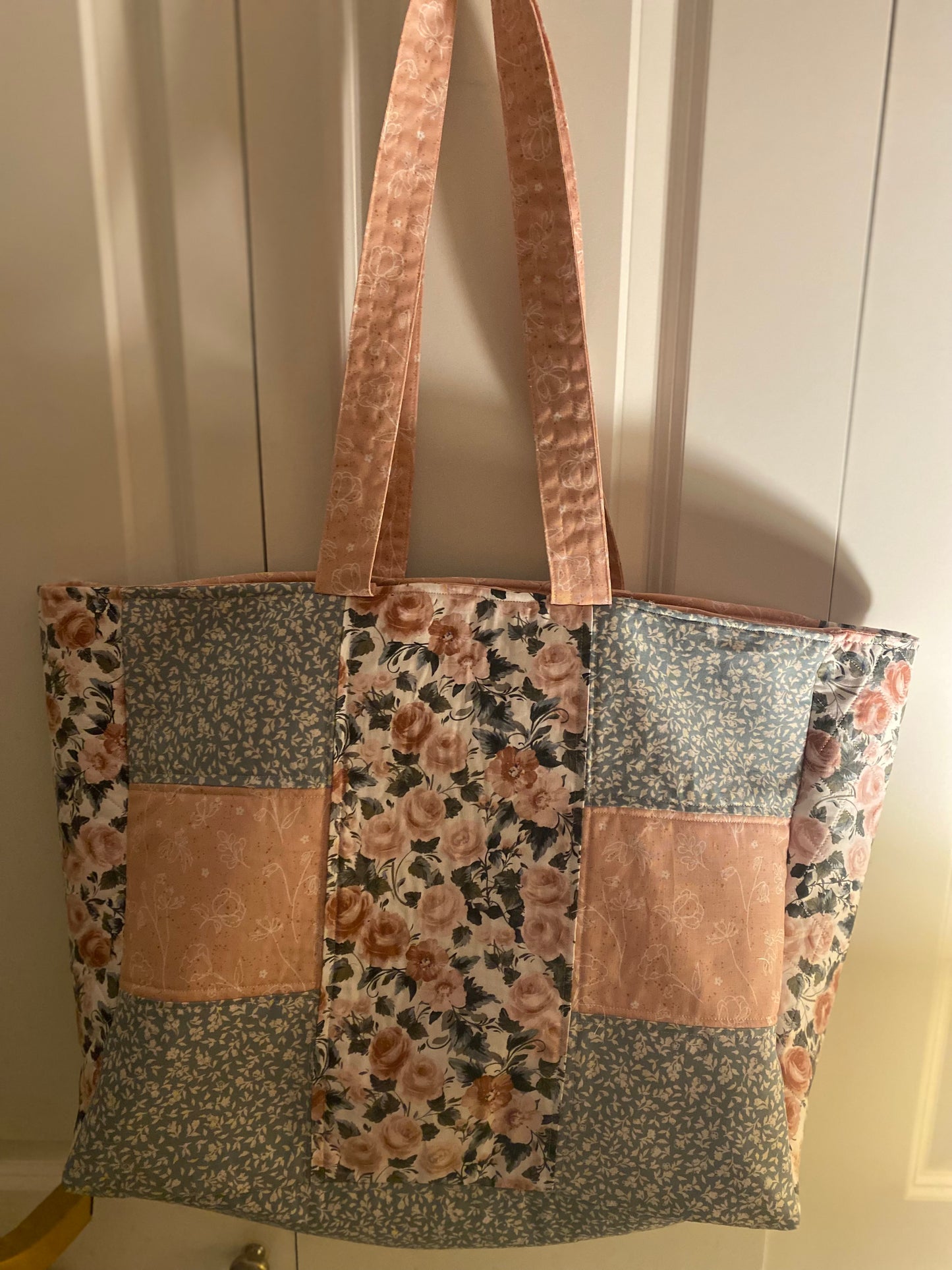 Patchwork tote bag with floral and floral-patterned fabric sections on a neutral background.