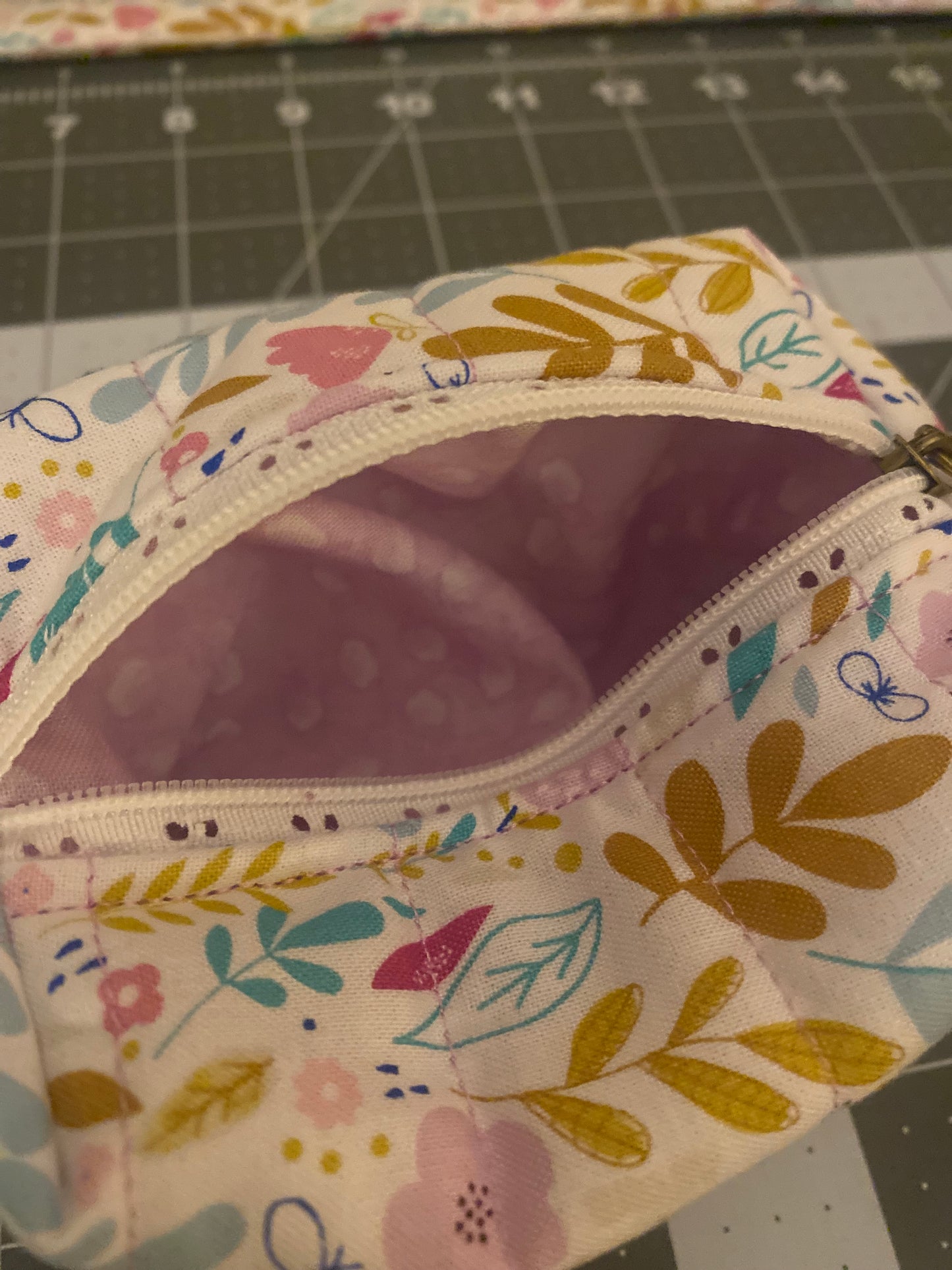 Floral-patterned fabric pouch with a zipper on a cutting mat background