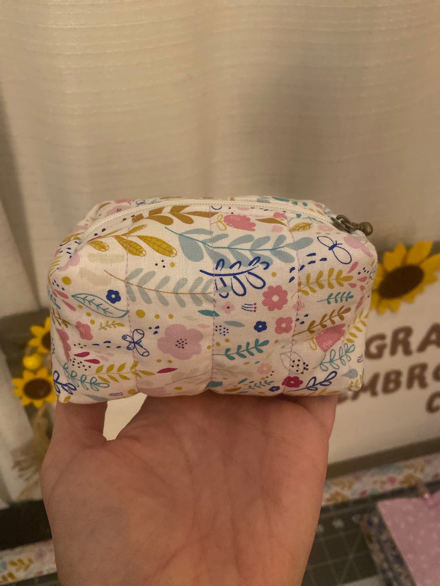 Floral-patterned pouch held in a hand with a blurred background
