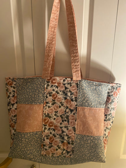 Patchwork tote bag with floral and floral-patterned fabric sections on a neutral background.