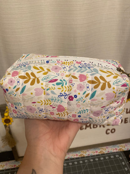 Floral-patterned pouch held by a hand with a neutral background